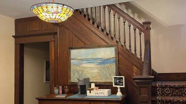 A wooden desk with a coffee maker, books, and a sign. A staircase with a railing is visible in the background.