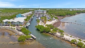 A marina with boats docked, a building with a blue roof, and a beach area with palm trees. - Overlooking The Marina and Ocean (Key Largo)
