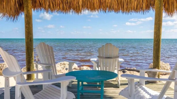 A wooden deck with white Adirondack chairs and a turquoise table, overlooking a calm sea. - Overlooking The Marina and Ocean (Key Largo)