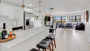 A modern kitchen with a large island, white cabinetry, and a dining area with black leather seating. - Overlooking The Marina and Ocean (Key Largo)