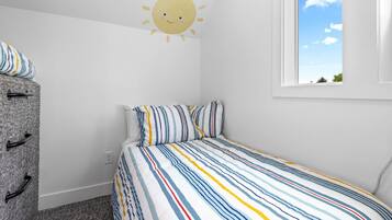 A bedroom with a striped bedspread, a dresser with black handles, and a wall decal of a smiling sun.