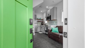 Una cocina moderna con gabinetes grises, un microondas y una estufa. En la sala de estar, hay un sofá de cuero marrón con un cojín azul verdoso.