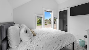 Un dormitorio con cama, televisor montado en la pared y vista al exterior a través de una puerta.