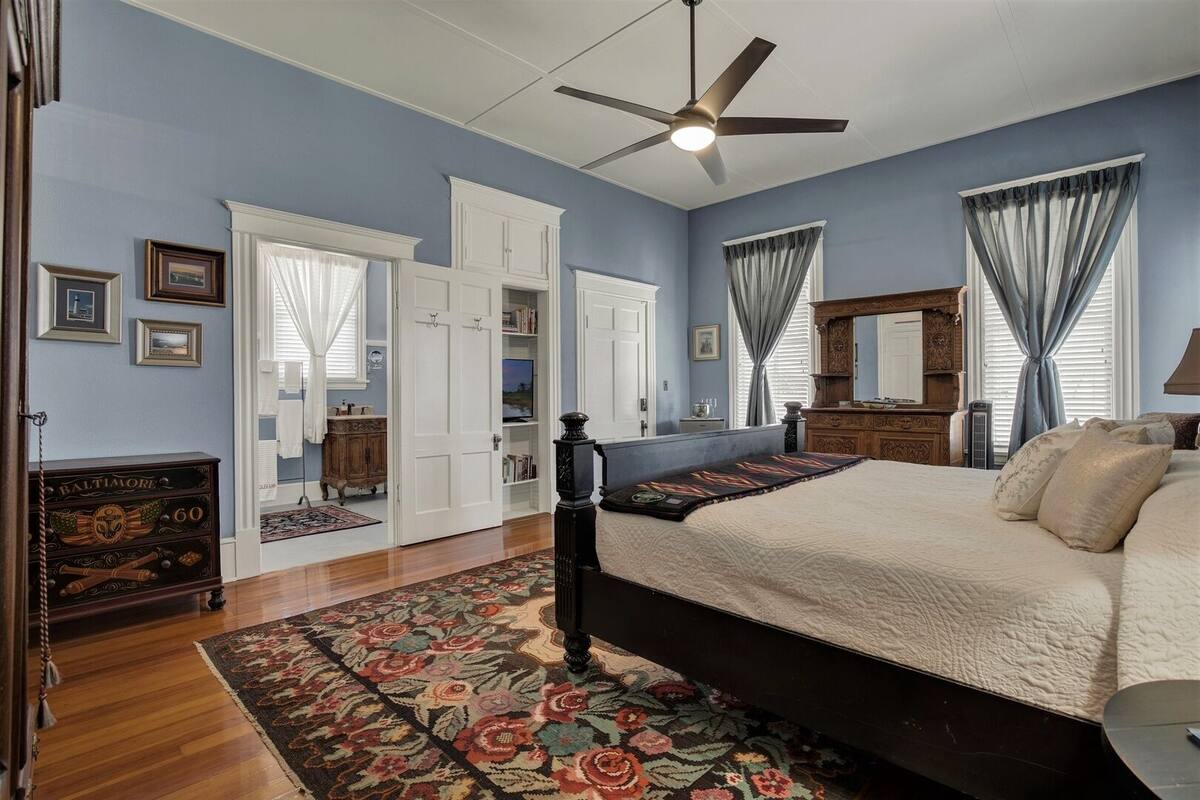 A bedroom with a bed, a ceiling fan, a dresser, a mirror, and a window with curtains.