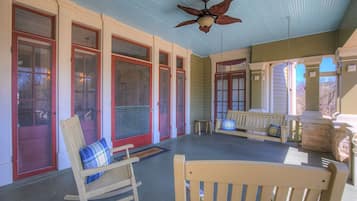 A covered porch with rocking chairs, a ceiling fan, and a stone fireplace.