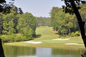 A golf course with a pond, sand bunkers, and a pavilion in the distance.