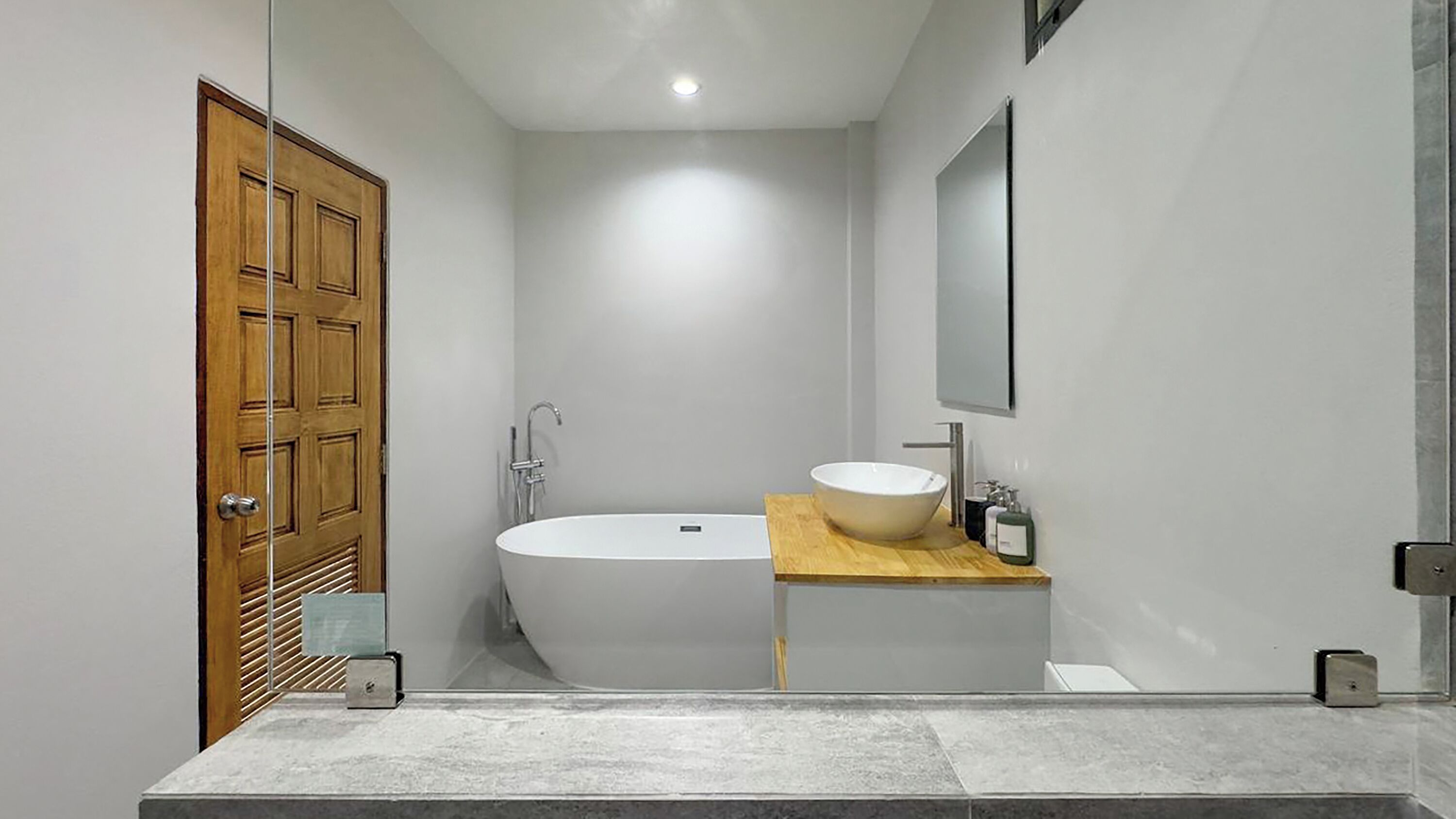 A modern bathroom with a freestanding bathtub, a wooden vanity, and a large mirror.