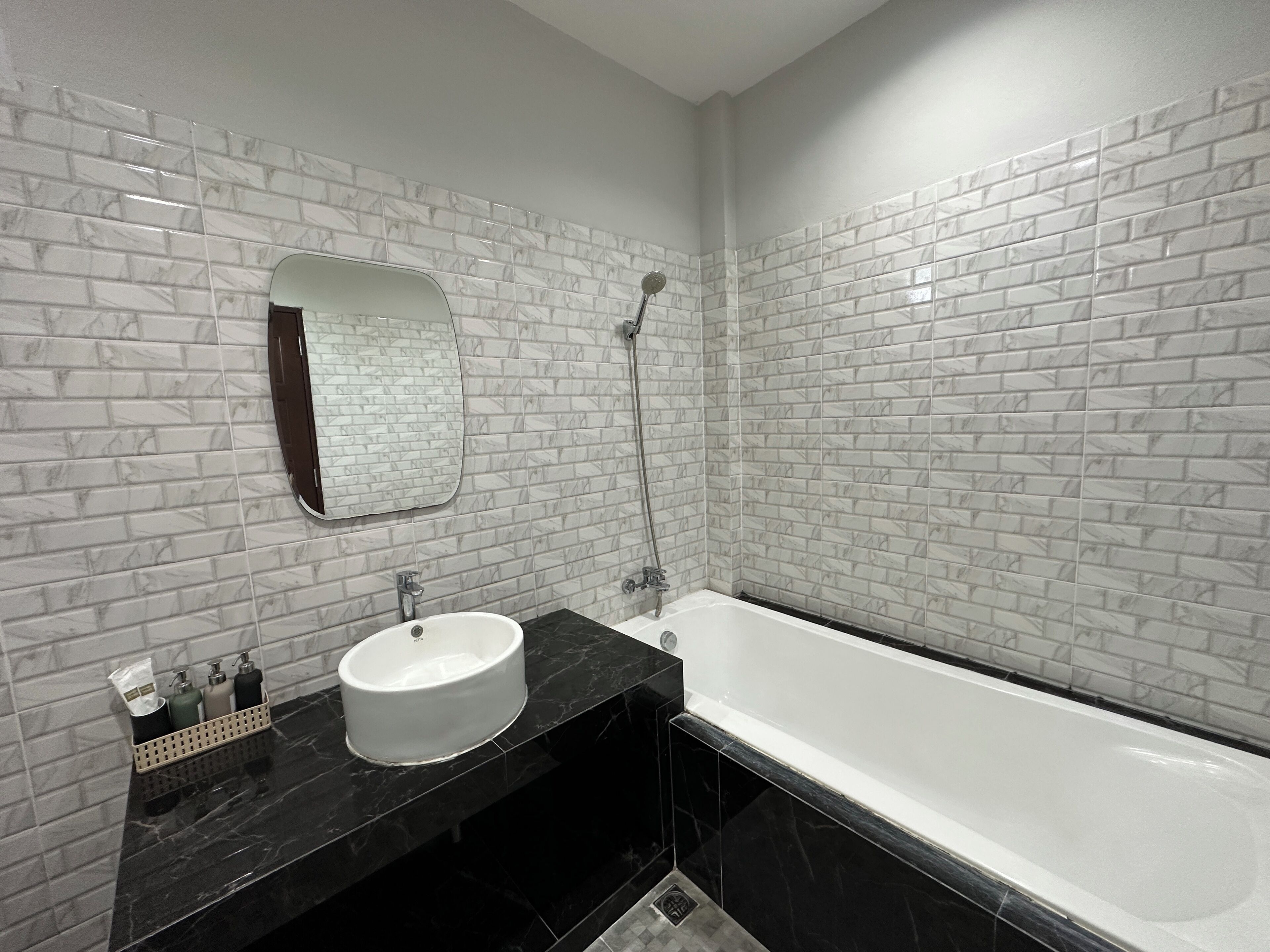 A modern bathroom with a white sink, black countertop, and a large bathtub.
