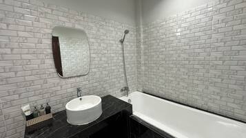 A modern bathroom with a white sink, black countertop, and a large bathtub.