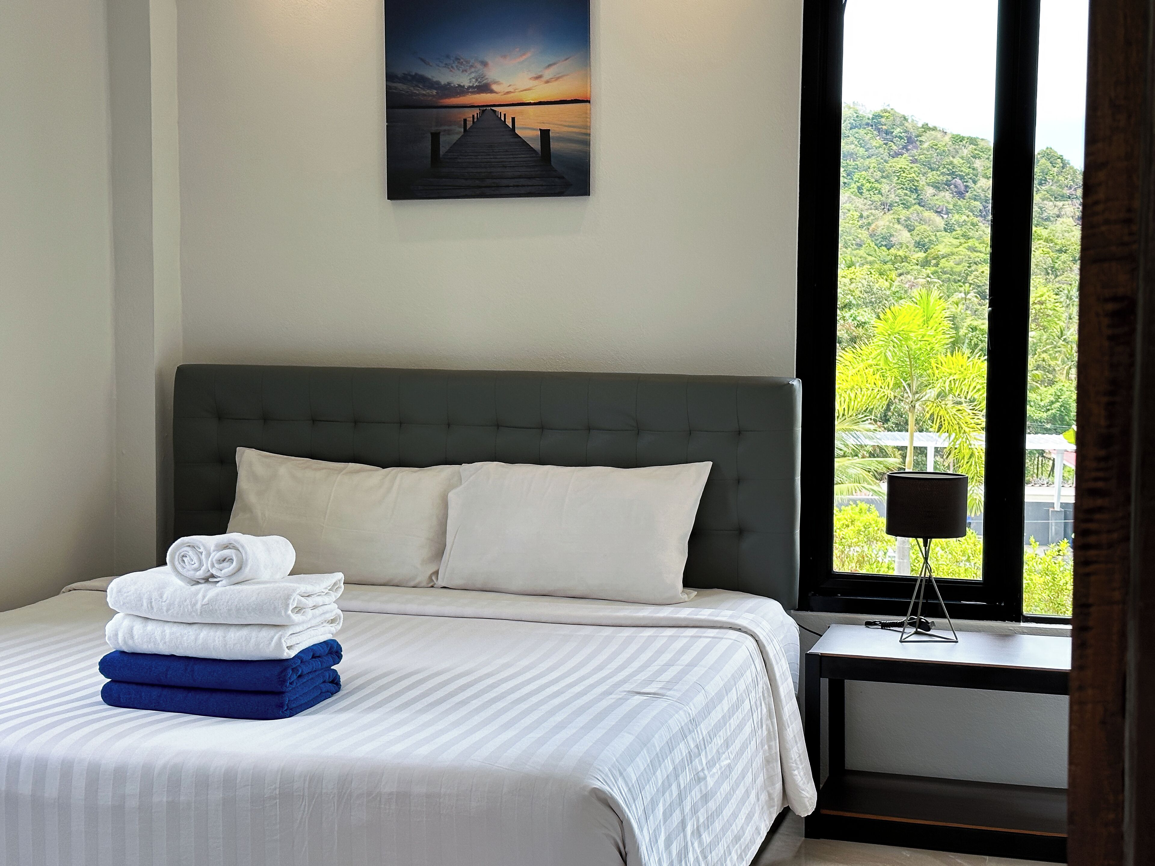 A neatly made bed with folded towels and a view of a sunset through a window.