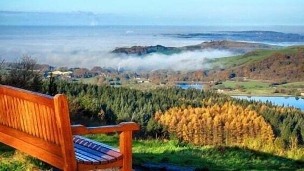 A wooden bench overlooking a scenic landscape with hills, a lake, and a misty horizon. - 2-Bed House in Macclesfield Cheshire (Macclesfield)