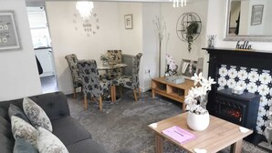 A living room with a sofa, chairs, a coffee table, a fireplace, and a dining area. - 2-Bed House in Macclesfield Cheshire (Macclesfield)