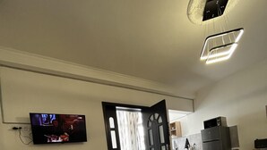 A modern living room with a flat-screen TV, a dining area with a table and chairs, a kitchen area with a refrigerator, and a wooden floor. - Opera Apartment Sleeps 4 with Patio (T'bilisi)