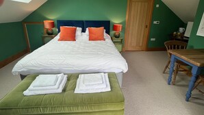 Een slaapkamer met een groot bed, groene wanden, een houten deur, een kleine tafel en een bank.