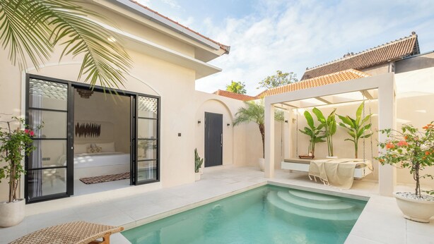 A modern pool area with a clear pool, lounge chairs, and a covered seating area with plants.