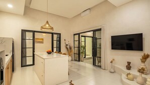A modern kitchen with a central island, a dining area with a round table, and a living room with a flat-screen TV.