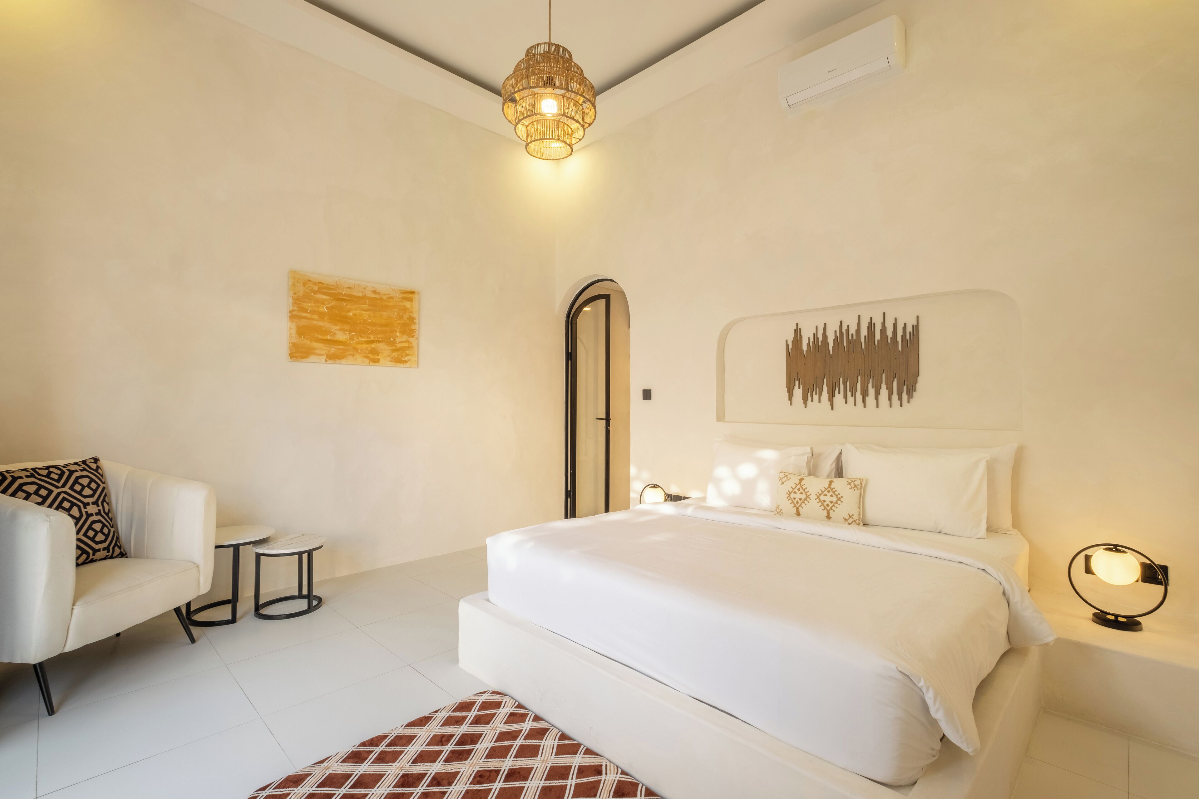 A modern bedroom with a large bed, a small side table, a sofa, and a unique wall art piece.