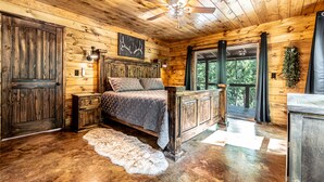 Un dormitorio de cabaña rústica con cama, paredes de madera, ventilador de techo y vistas al exterior.