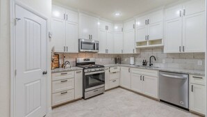 Una cocina moderna con armarios blancos, electrodomésticos de acero inoxidable y salpicadero de azulejos.