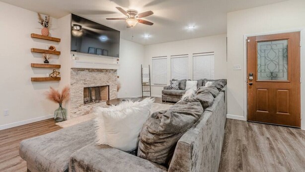 Una sala de estar moderna con chimenea, un sofá modular, estantes de madera y un ventilador de techo.