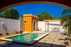 A swimming pool with a stone deck, a small orange building, and a white wall with a patterned section. - Casa Flamingos Altabi (Mérida)