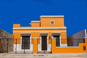 A two-story building with a flat roof, a central entrance with a black door, and a small circular window above the door. - Casa Flamingos Altabi (Mérida)