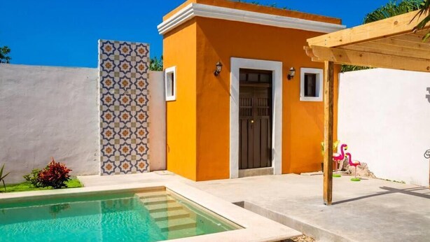 Ein kleines Gebäude mit Pool, einer Pergola und einer Kachelwand.