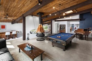 Un grand espace de vie comprenant une table de billard, une cheminée et un coin repas avec un banc et une table.