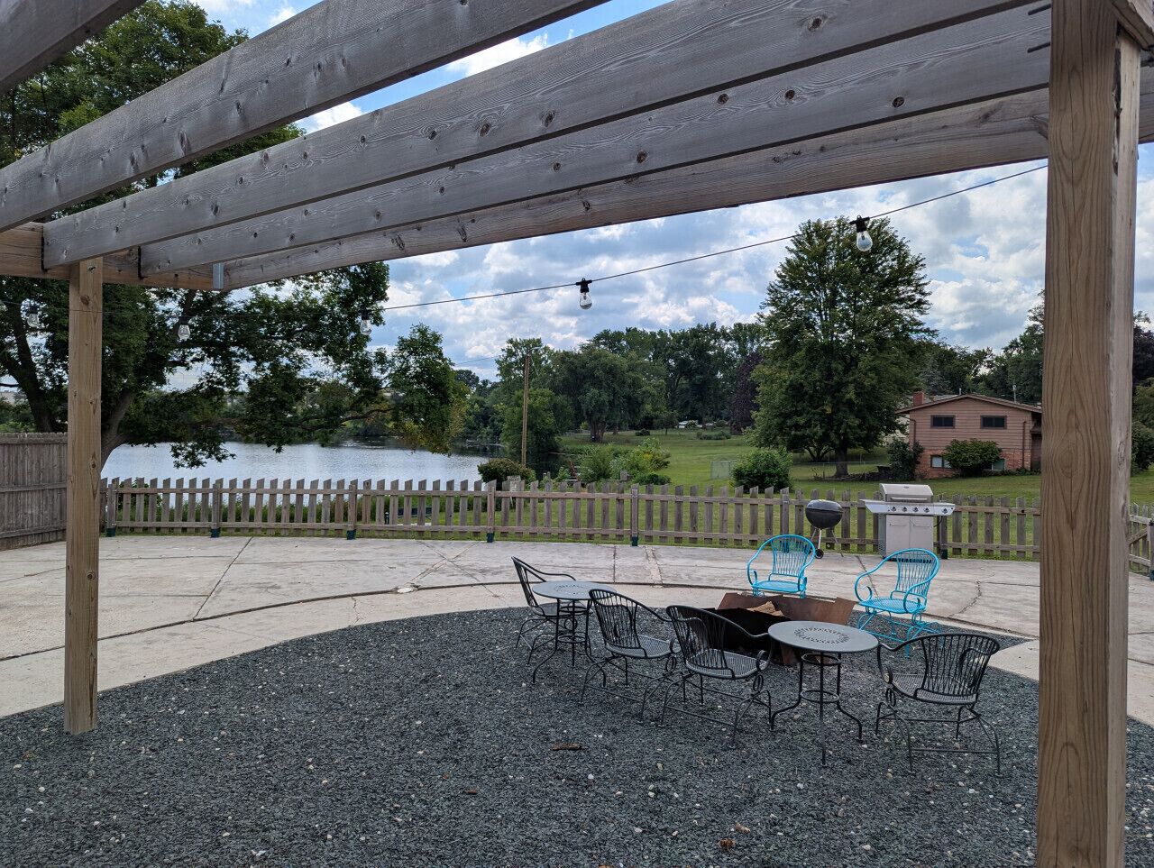 Eine Terrasse im Freien mit einer Pergola, einem Grill und einem Tisch mit Stühlen.