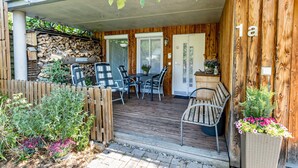 En overdækket terrasse med træterrasse, et bord og stole, en bænk og en blomsterkasse.