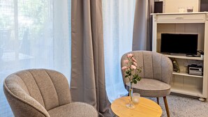 En stue med to lænestole, et rundt sofabord med en vase, og et fjernsyn på et hvidt skab.
