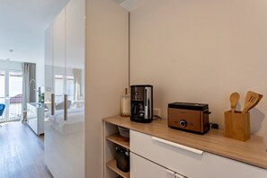 Une petite cuisine équipée d’une machine à café, d’un grille-pain et d’un porte-ustensiles en bois, le tout posé sur un plan de travail en bois.