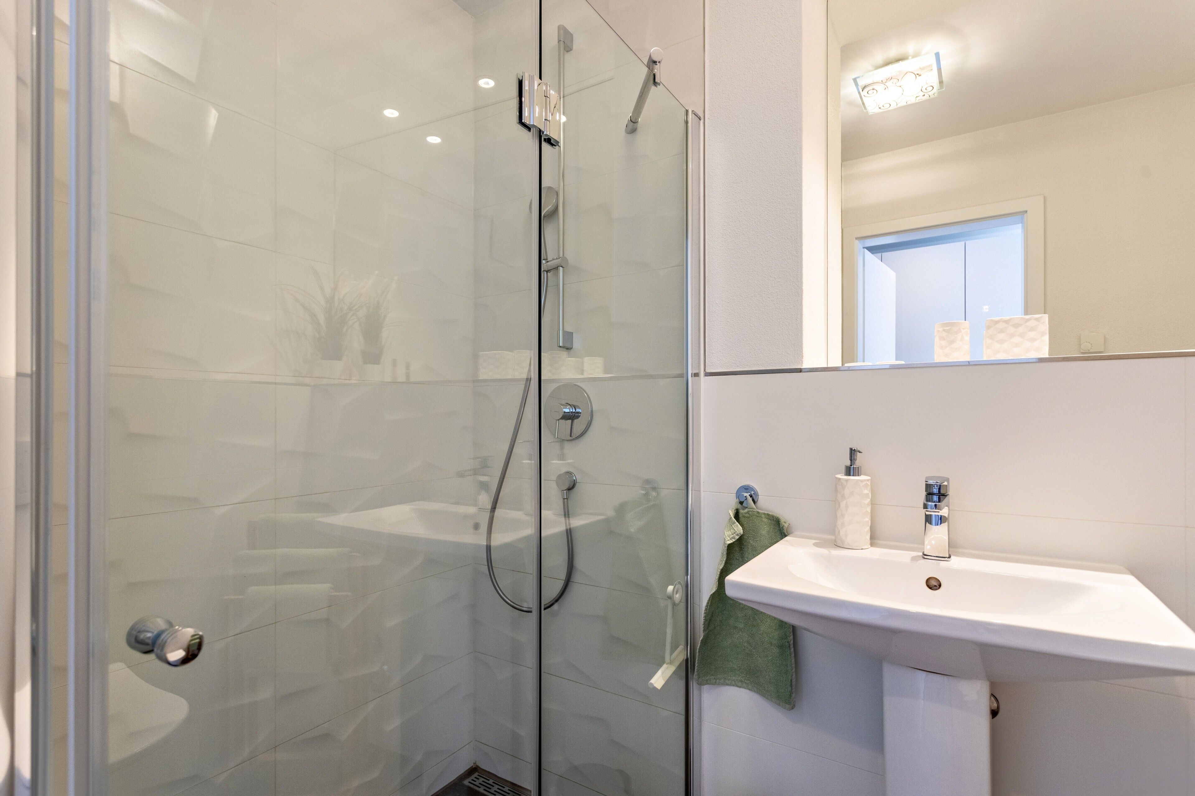Een moderne badkamer met een douche in een glazen cabine, een witte wastafel en een spiegel erboven.