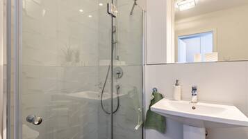 Een moderne badkamer met een douche in een glazen cabine, een witte wastafel en een spiegel erboven.