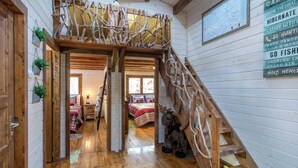 Una escalera de madera con diseño rústico que lleva a un dormitorio en entrepiso con colcha de cuadros rojos y blancos.