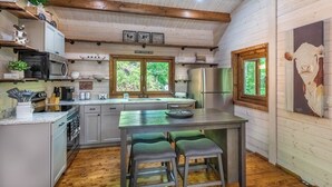 Cocina rústica con vigas de madera, una isla central con taburetes y un letrero que dice 'Family Gather Here'.