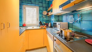 Une cuisine avec des carreaux de céramique bleu-vert et jaune, des appareils électroménagers en acier inoxydable et une fenêtre.
