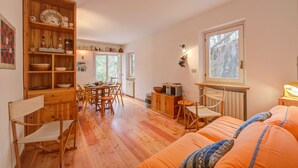 Une pièce chaleureuse avec une table à manger en bois, des chaises, un canapé et un coin cuisine doté de meubles en bois et d’une fenêtre.