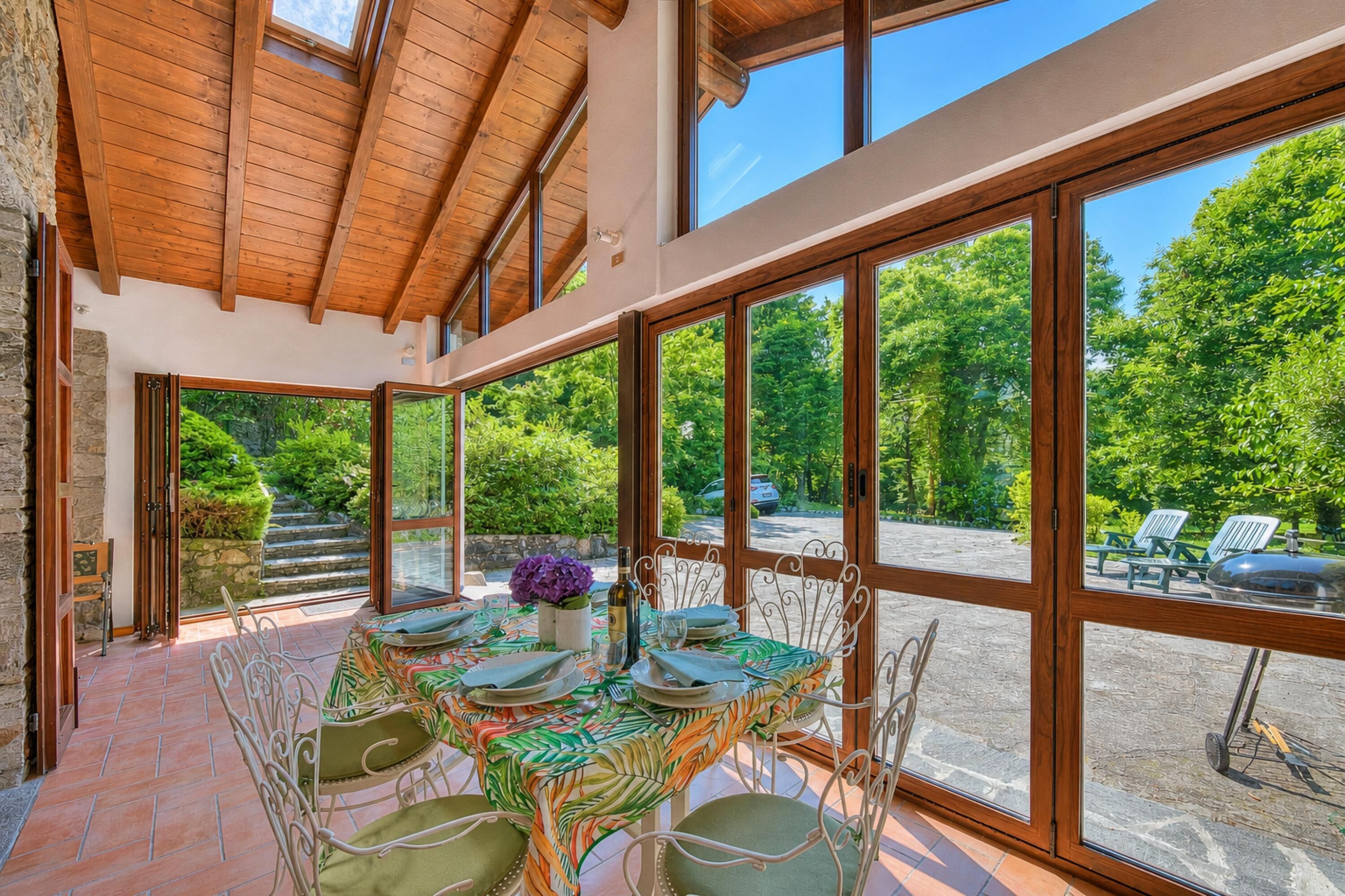 A dining area with a table set for six, large windows, and a view of greenery outside.
