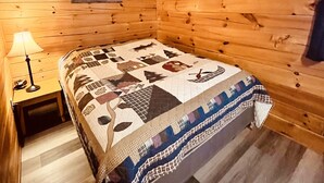 Een gezellig houten kamer met een bed met quilt, een nachtkastje met lamp en een lijst met foto aan de muur.