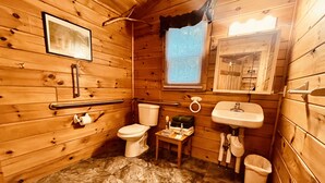 Een knus houten badkamertje met toilet, wastafel en een klein tafeltje met toiletartikelen.