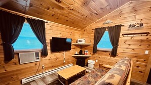 Een houten chalet van binnen, met een bank, een flatscreen-tv, een magnetron en een kleine tafel.