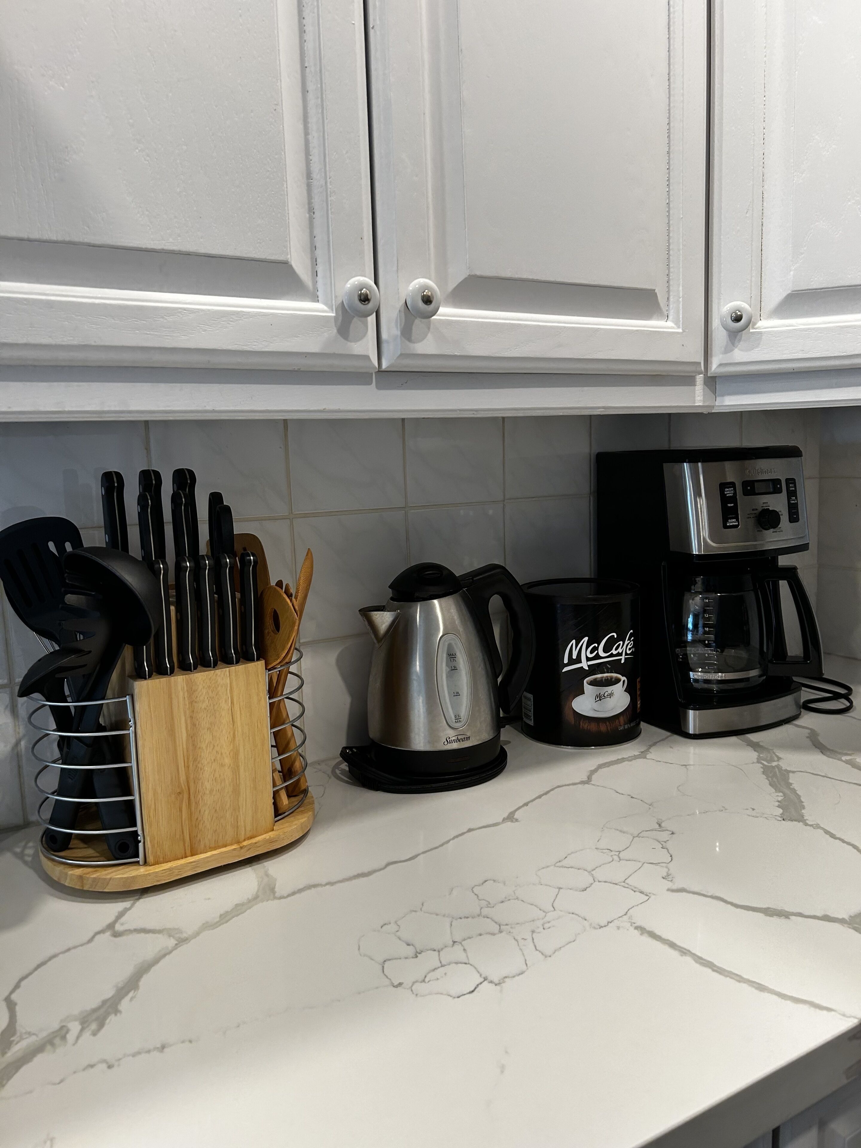 Una encimera de cocina con una cafetera, un bote de McCafé, un hervidor y un bloque de cuchillos.
