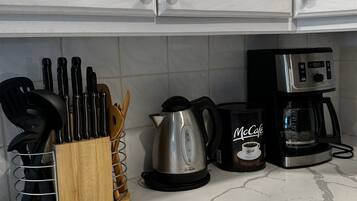 Una encimera de cocina con una cafetera, un bote de McCafé, un hervidor y un bloque de cuchillos.
