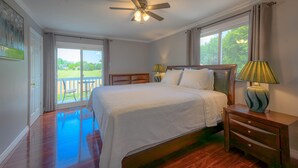 A bedroom with a large bed, a ceiling fan, a nightstand, a lamp, and a view of a balcony. - Entire House with pool in Niagara-on-the-lake close to Niagara Falls (Niagara-on-the-Lake)