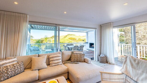 A modern living room with a large sectional sofa, a wicker chair, and a view of the outdoors. - Oriwa Villa Oneroa near Mudbrick (Waiheke Island)