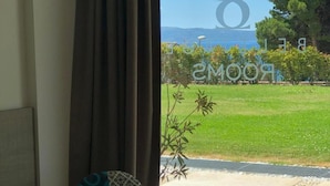 Ein Zimmer mit Blick auf eine grüne Wiese und ein Gewässer. Ein Sessel mit gemustertem Kissen und ein Tisch sind ebenfalls vorhanden.