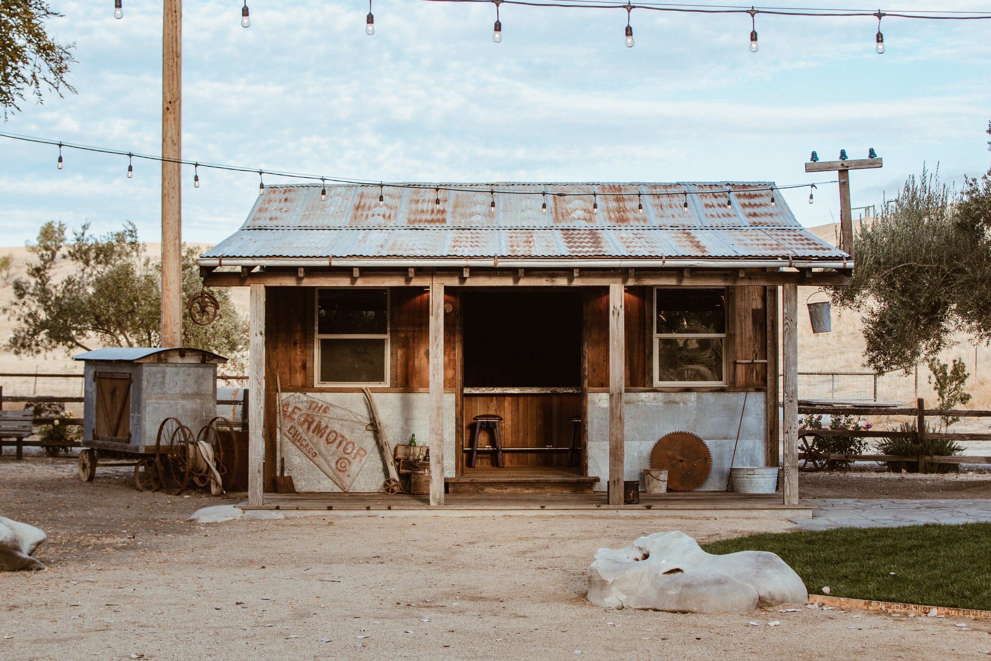 A rustic, single-story building with a corrugated metal roof, a wooden door, and a sign that reads "The Berm Motor Co."