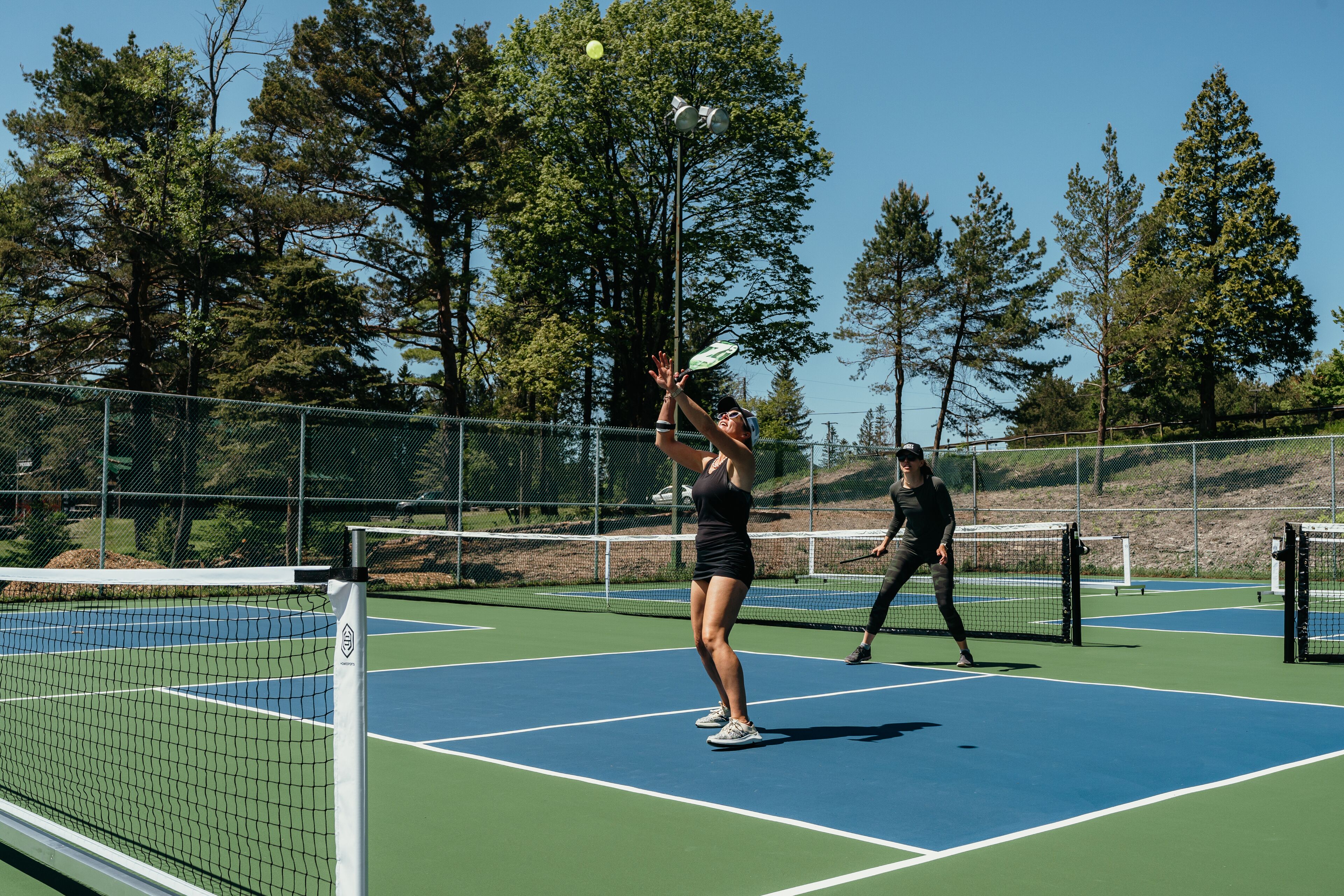 Cancha de tenis con red, rodeada de árboles y una valla.