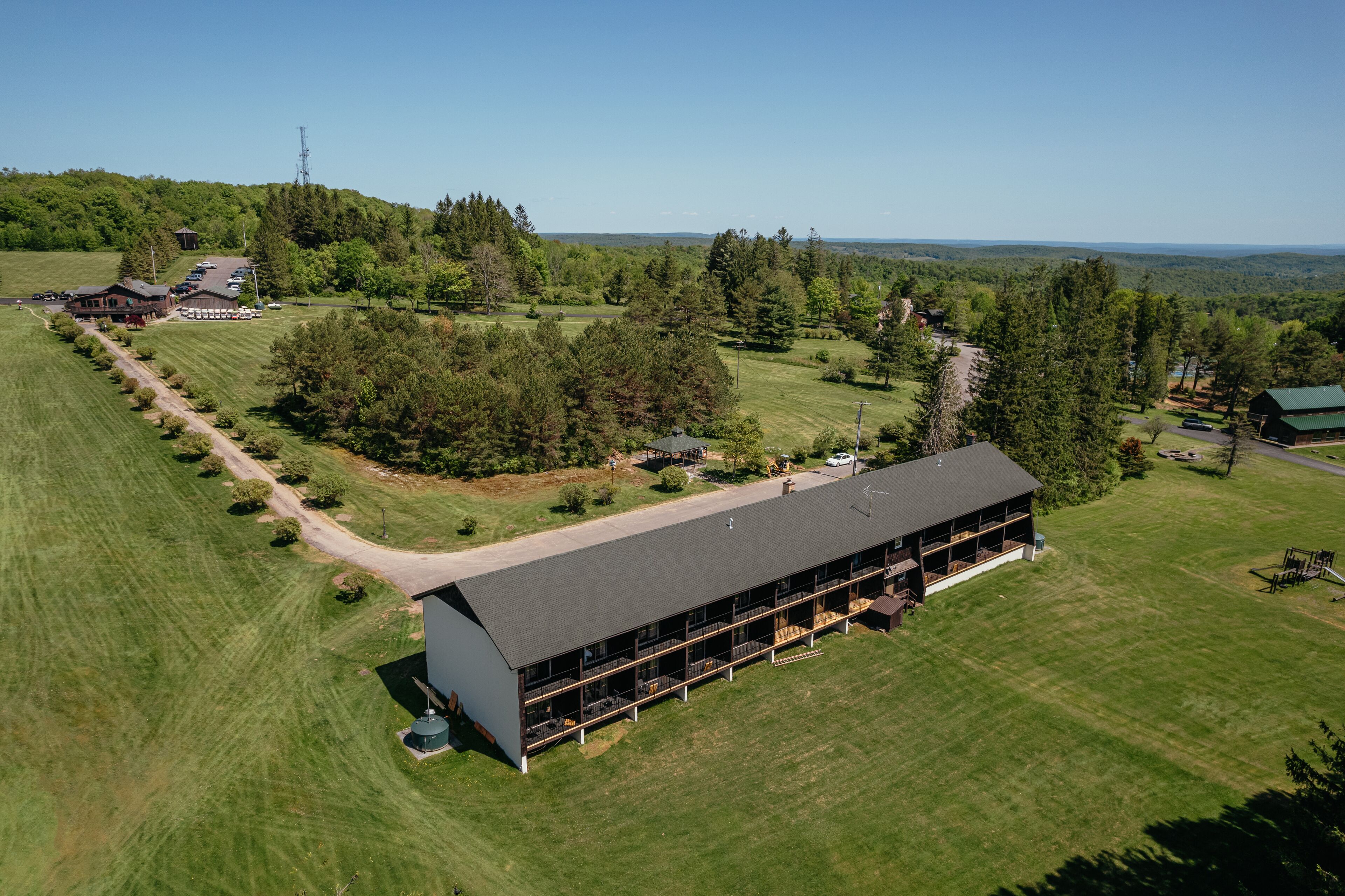 A large, modern building with a flat roof and multiple balconies, surrounded by well-maintained lawns and trees.